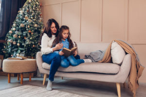 Mother and daughter read book on couch near Christmas tree