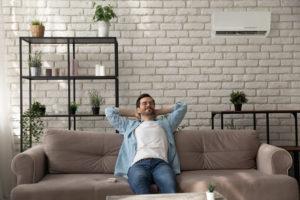 Man sits on couch comfortably underneath his ductless cooling and heating unit