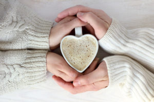 people wearing white sweaters hold hands around a heart-shaped mug of cocoa