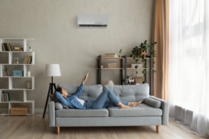 woman lying on couch using remote to operate ductless ac