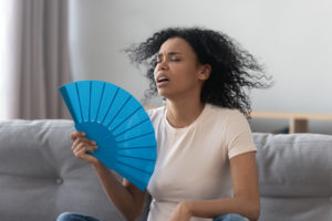 woman sits on couch and uses fan during heatwave