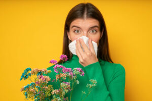 woman with spring flowers sneezes into tissue