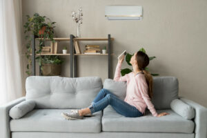 girl adjusts ductless unit while sitting on sofa in front of window