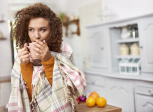 Young woman wrapped in blanket drinking hot tea