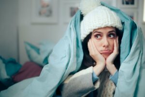 woman wearing hat and covered in blanket is unhappy in chilly home