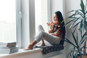 young woman enjoying her bouquet of tulips while resting on the window sill at home
